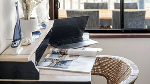Ein Arbeitsplatz mit Laptop, Papierkram und Dekorationen an einem Fenster mit Blick auf eine Küstenlandschaft.