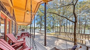 Een houten terras met rode Adirondack stoelen, een hangmat en uitzicht op een meer en bomen.