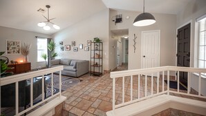 A spacious living area with a grey sofa, a black bookshelf, and a white railing. - Casa Leon: 4BR House w/ Pool near Strip! (Las Vegas)