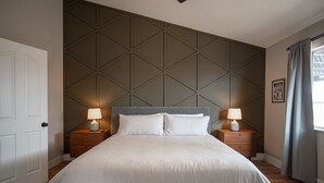 A neatly made bed with white linens, two bedside tables with lamps, a wooden headboard, and a geometric-patterned wall. - Casa Leon: 4BR House w/ Pool near Strip! (Las Vegas)