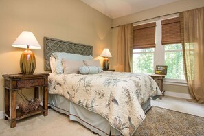 Een slaapkamer met een bed, twee nachtkastjes met lampen, een raam met gordijnen en een ingelijst schilderij aan de muur.