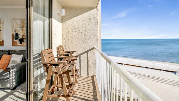 A balcony with wooden furniture, a glass door, and a view of the beach. - Beachfront @ Seaside Beach & Racquet 1BR • Sleeps 4 • Amazing Views (Orange Beach)