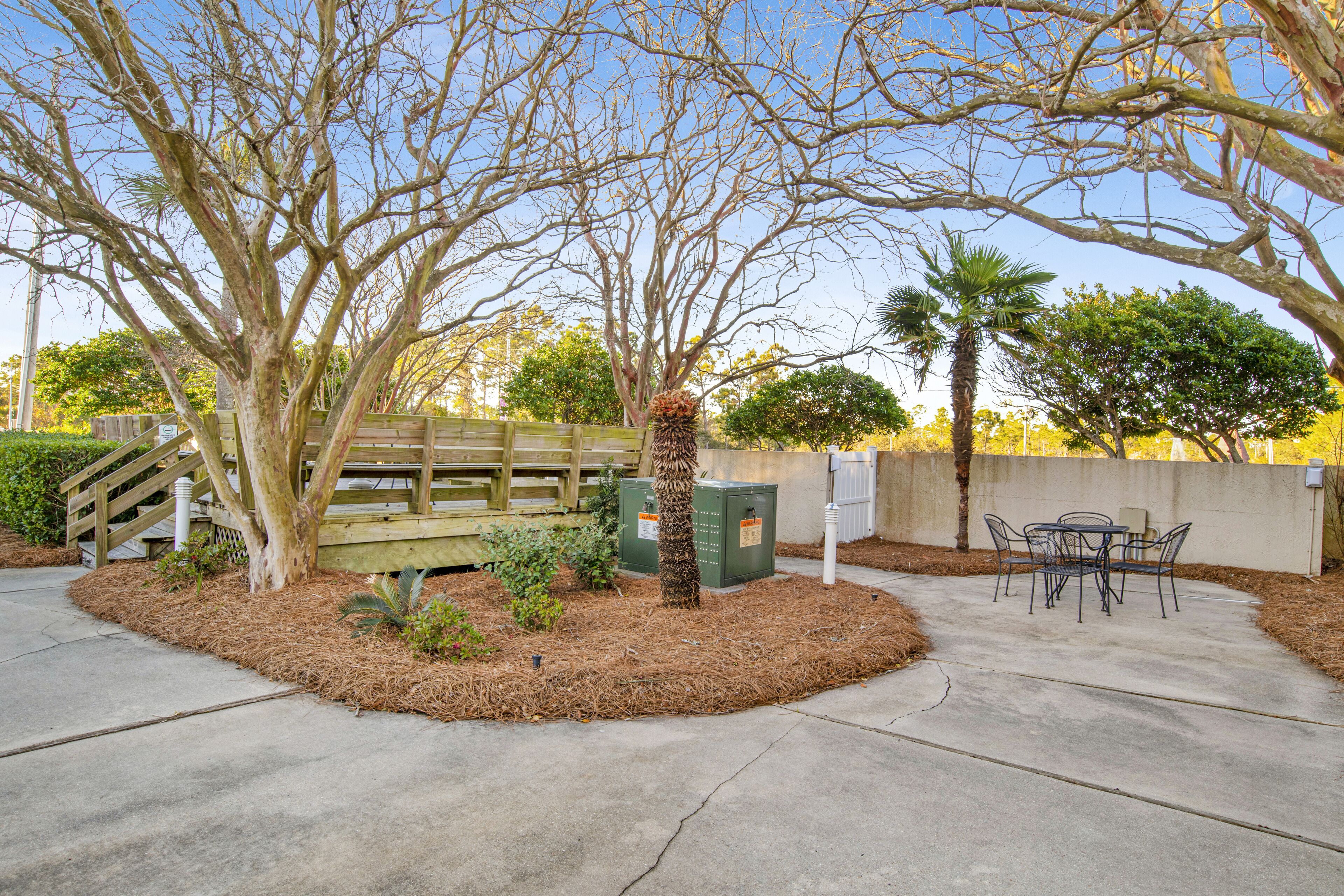 A patio area with a wooden table and chairs, surrounded by trees and a wooden fence.