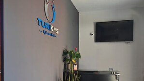Ein Empfangsbereich mit einer schwarzen Ledersofa, einem Blumentopf, einem an der Wand montierten Fernseher und einer Rezeption.