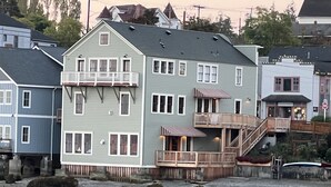 Un edificio de dos pisos con un balcón, una terraza de madera y una escalera que lleva a un nivel superior.