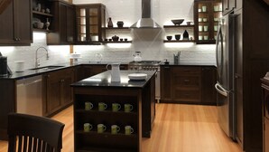Una cocina moderna con armarios de madera oscura, una isla central con pileta y un refrigerador de acero inoxidable.