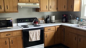 A kitchen with wooden cabinets, a stove, a microwave, and a ceiling fan. - Farmhouse - in the country but close to everything. 4 bedrooms-Sleeps 10 (Independence)