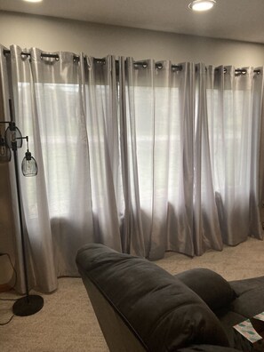 A living room with a large window covered by sheer curtains, a black floor lamp, and a dark-colored sofa.