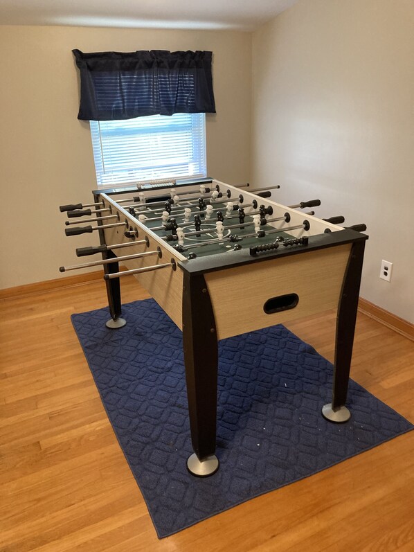A foosball table in a room with wooden flooring and a blue rug.