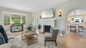 A spacious living room with a fireplace, comfortable seating, and a view of the kitchen.