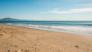 A beach with a clear sky, calm sea, and distant mountains.