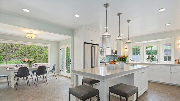 A modern kitchen with white cabinetry, a large island with bar stools, stainless steel appliances, and pendant lighting.