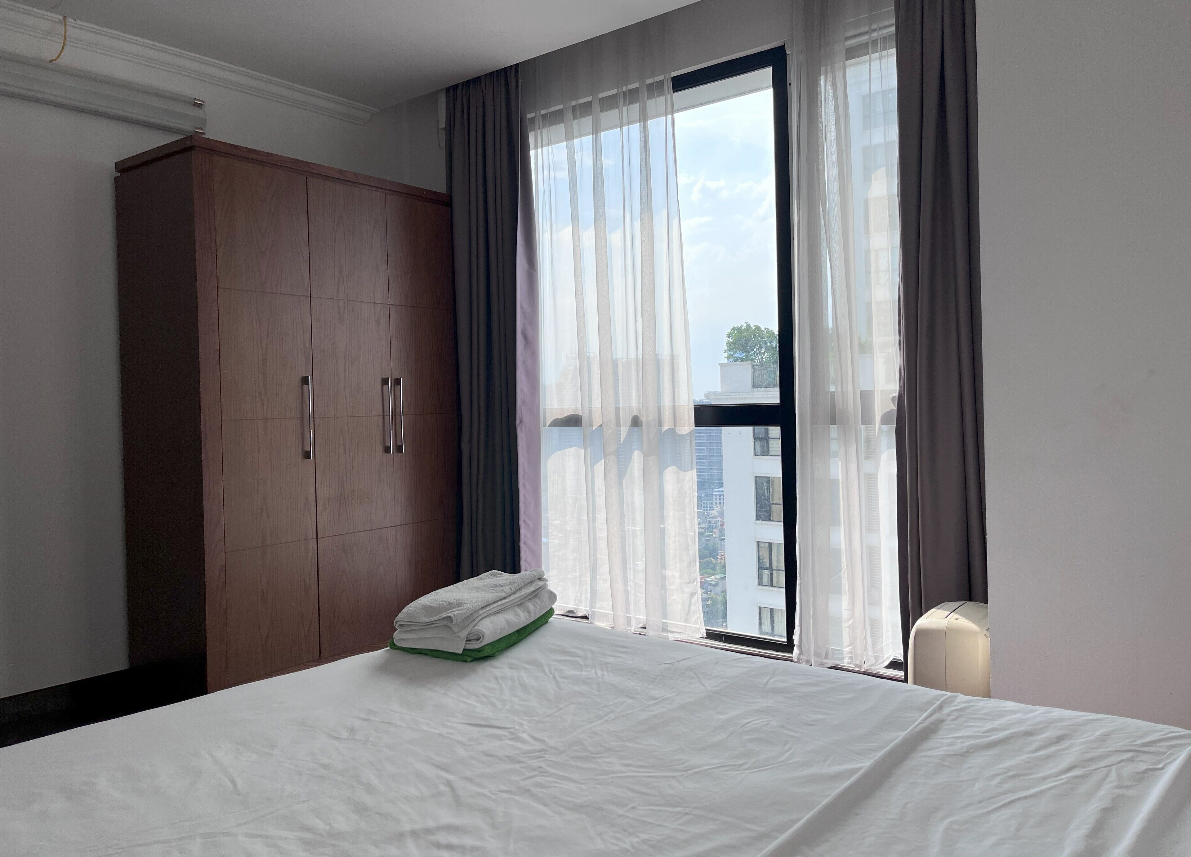 Een hotelkamer met een groot bed, een kledingkast en een raam met gordijnen.