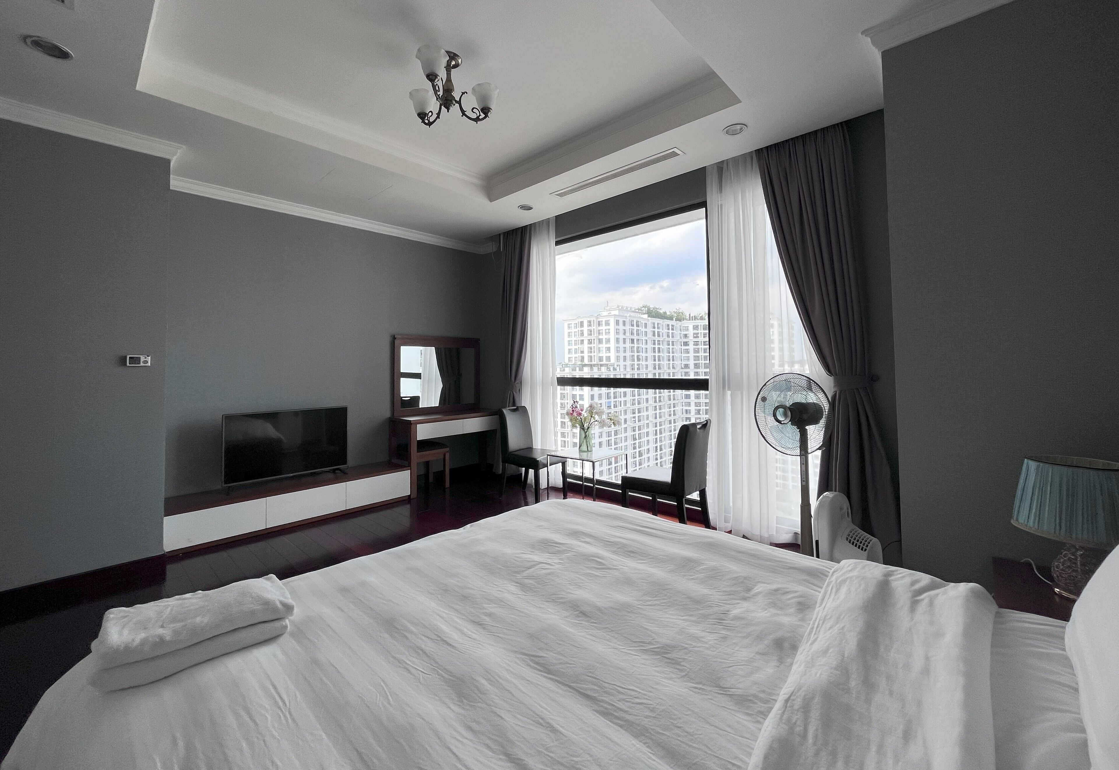 A modern hotel room with a large bed, a desk, a TV, and a view of the city.