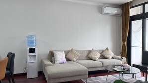 A modern living room with a sofa, a coffee table, a water dispenser, and a large window with curtains.