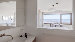 A modern bathroom with a large mirror, a sink, and a window overlooking the sea. - Appartement Ocean Suite - Ocean Suite (Wenningstedt-Braderup (Sylt))