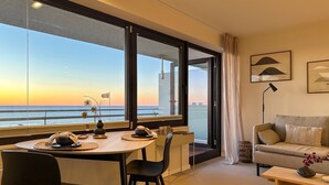 A modern living room with a dining area, large windows with a view of the sea, a sofa, and a lamp. - Appartement Ocean Suite - Ocean Suite (Wenningstedt-Braderup (Sylt))