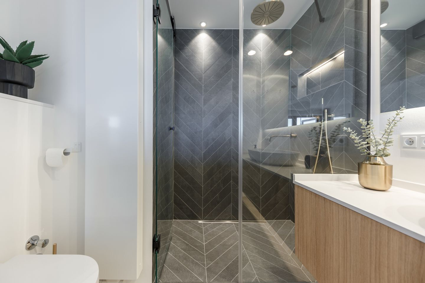 A modern bathroom with a glass shower enclosure, a white sink, and a wooden vanity.