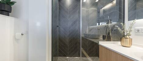 A modern bathroom with a glass shower enclosure, a white sink, and a wooden vanity.