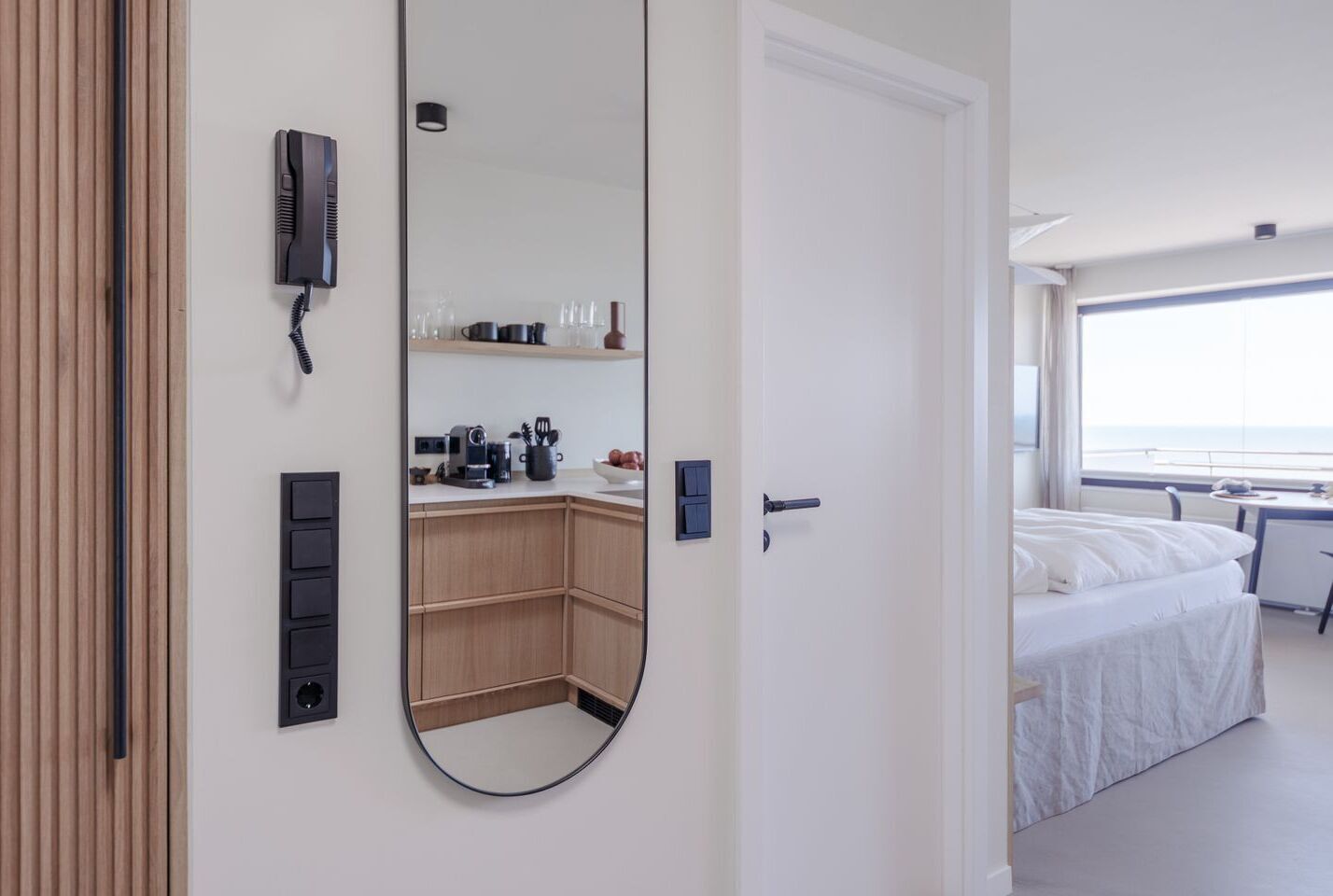 A hotel room with a large mirror, a bed, a desk, and a view of the sea.