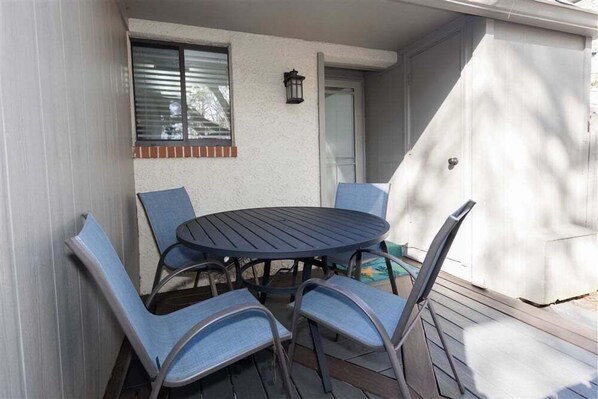 Eine Terrasse mit rundem Tisch und vier Stühlen, ein Fenster mit Jalousien und eine Tür.