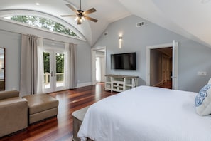 A spacious bedroom with a large bed, a ceiling fan, a TV, and a view of the outdoors.