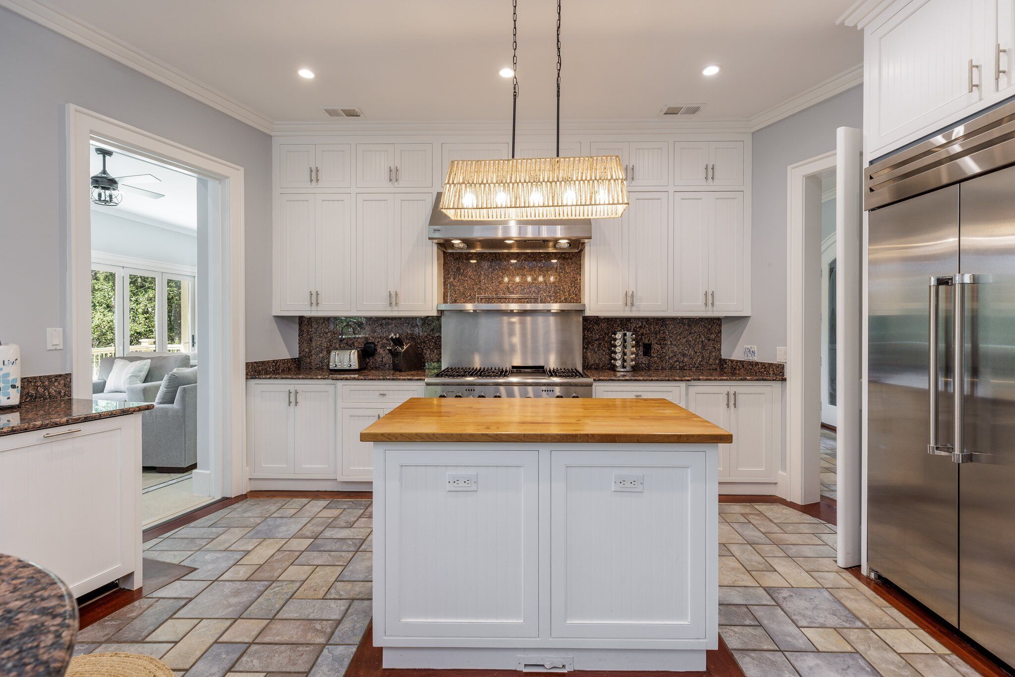 Una cocina moderna con armarios blancos, una isla de madera, electrodomésticos de acero inoxidable y una lámpara colgante.