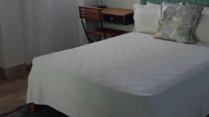 A bedroom with a bed, a desk, a chair, a window with curtains, and a wall-mounted air conditioner. - TonLin Pewee Drive 1 Bedroom (Gros Islet)