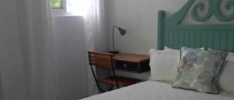 Un dormitorio con cama, escritorio, silla, ventana con cortinas y aire acondicionado instalado en la pared.