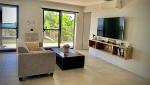 Een moderne woonkamer met een bank, salontafel, televisie en een balkon met uitzicht op groen.