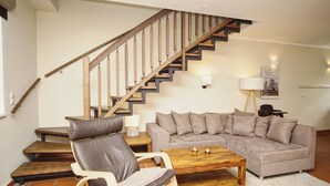 Ein Wohnzimmer mit einer Holztreppe, einem grauen Sofa, einem Holztisch und einem Ledersessel.
