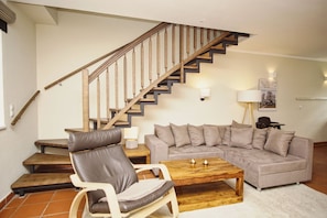Ein Wohnzimmer mit einer Holztreppe, einem grauen Sofa, einem Holztisch und einem Ledersessel.