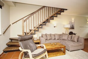 A living room with a wooden staircase, a grey sofa, a wooden coffee table, and a leather armchair.