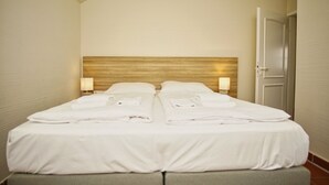 Ein Doppelbett mit ordentlich gefalteten weißen Handtüchern, einem Holzkopfteil und zwei Nachttischlampen.