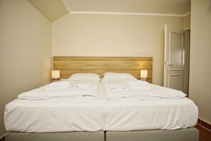 Ein Doppelbett mit ordentlich gefalteten weißen Handtüchern, einem Holzkopfteil und zwei Nachttischlampen.