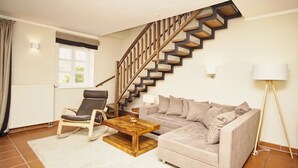 Ein Wohnzimmer mit einer Holztreppe, einem Sofa, einem Sessel, einem Couchtisch und einer Stehlampe.