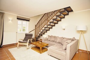 Ein Wohnzimmer mit einer Holztreppe, einem Sofa, einem Sessel, einem Couchtisch und einer Stehlampe.