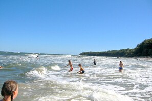 Ein Strand mit badenden und spielenden Menschen im Wasser.