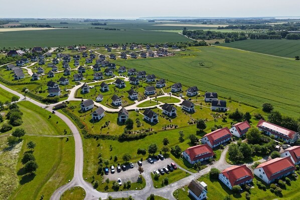 Vogelperspektive eines Wohngebiets mit in Kreismuster angeordneten Häusern, umgeben von grünen Feldern und einigen größeren Gebäuden mit roten Dächern.