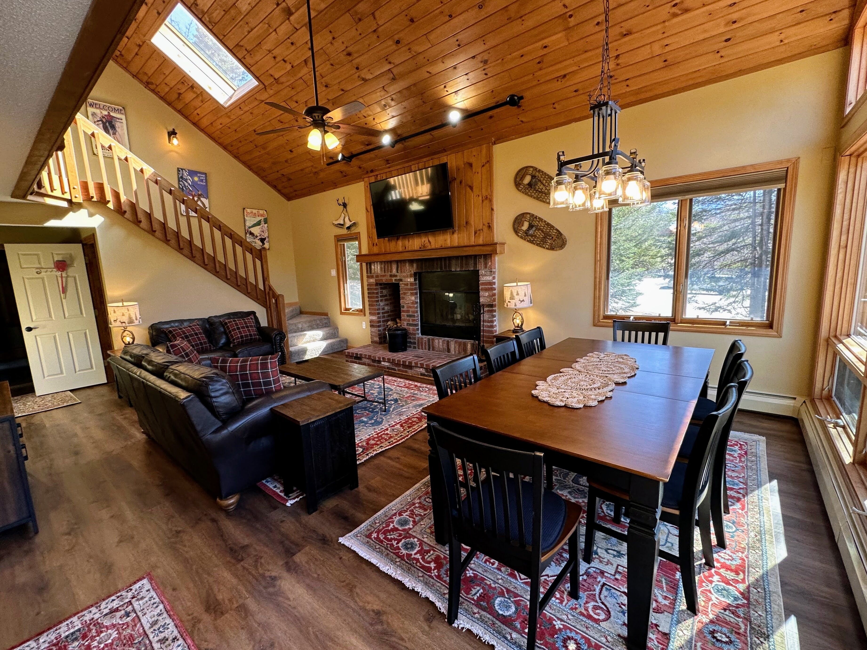 A spacious living area with a wooden ceiling, a fireplace, a television, and a dining table with chairs.