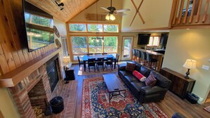 A spacious living room with a fireplace, a large rug, a leather sofa, and a dining area with a view of the outdoors. - MWP25 Updated 3 bed 3 bath condo with mountain ski slope views in Bretton Woods (Bretton Woods)