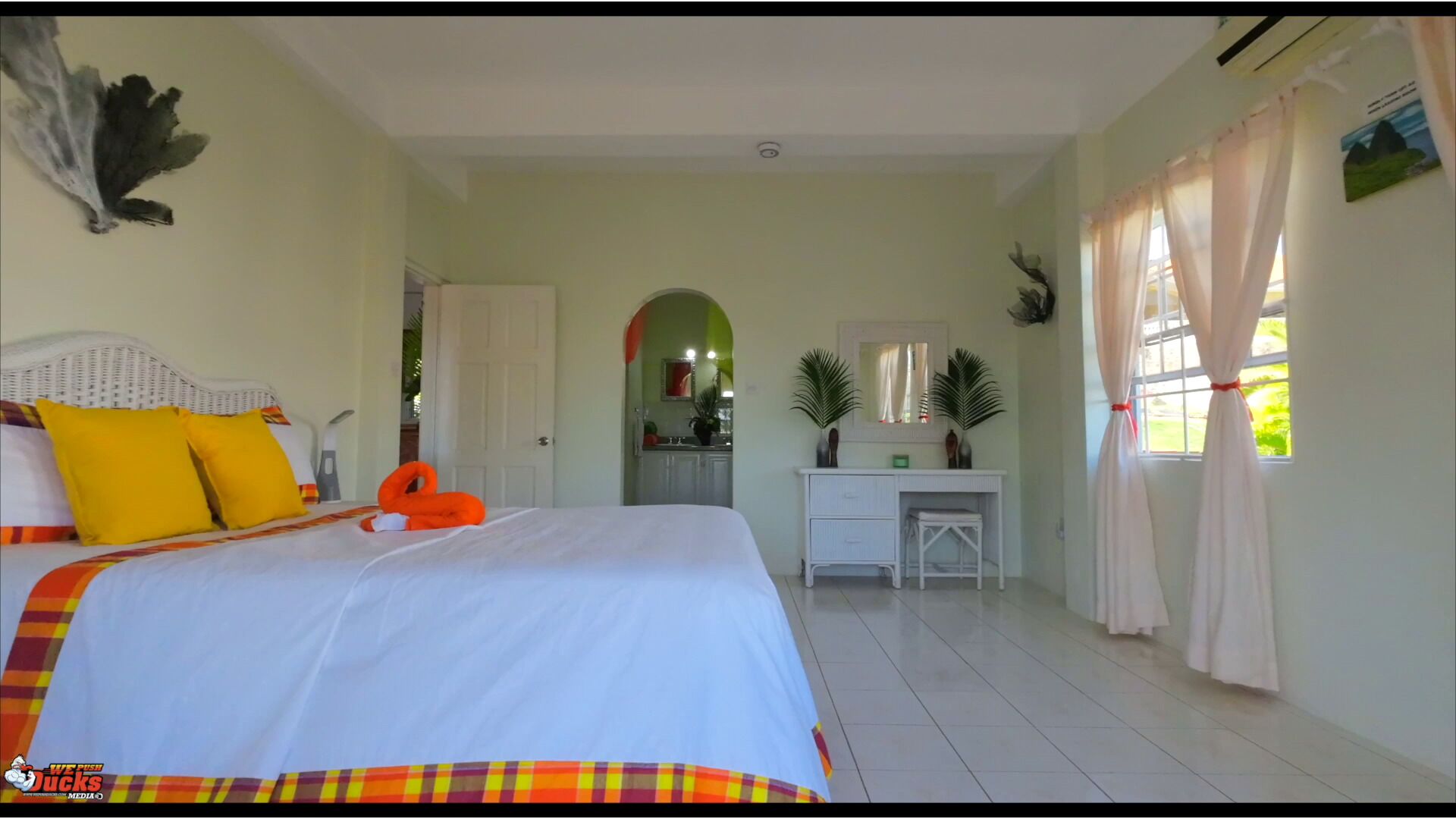 A bedroom with a bed, a desk, and a view of the kitchen.