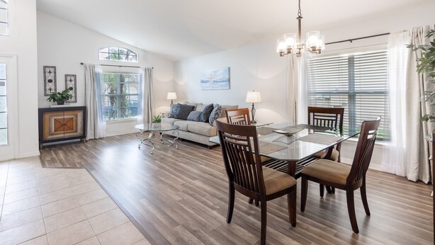 A spacious living room with a dining area, featuring a large glass table, wooden chairs, a sofa, and a fireplace. - Aviana resort near Disney, private pool, WiFi, washer, dryer, gameroom (Davenport)
