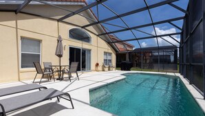 A swimming pool with a glass enclosure, lounge chairs, and a patio area with a table and chairs. - Aviana resort near Disney, private pool, WiFi, washer, dryer, gameroom (Davenport)