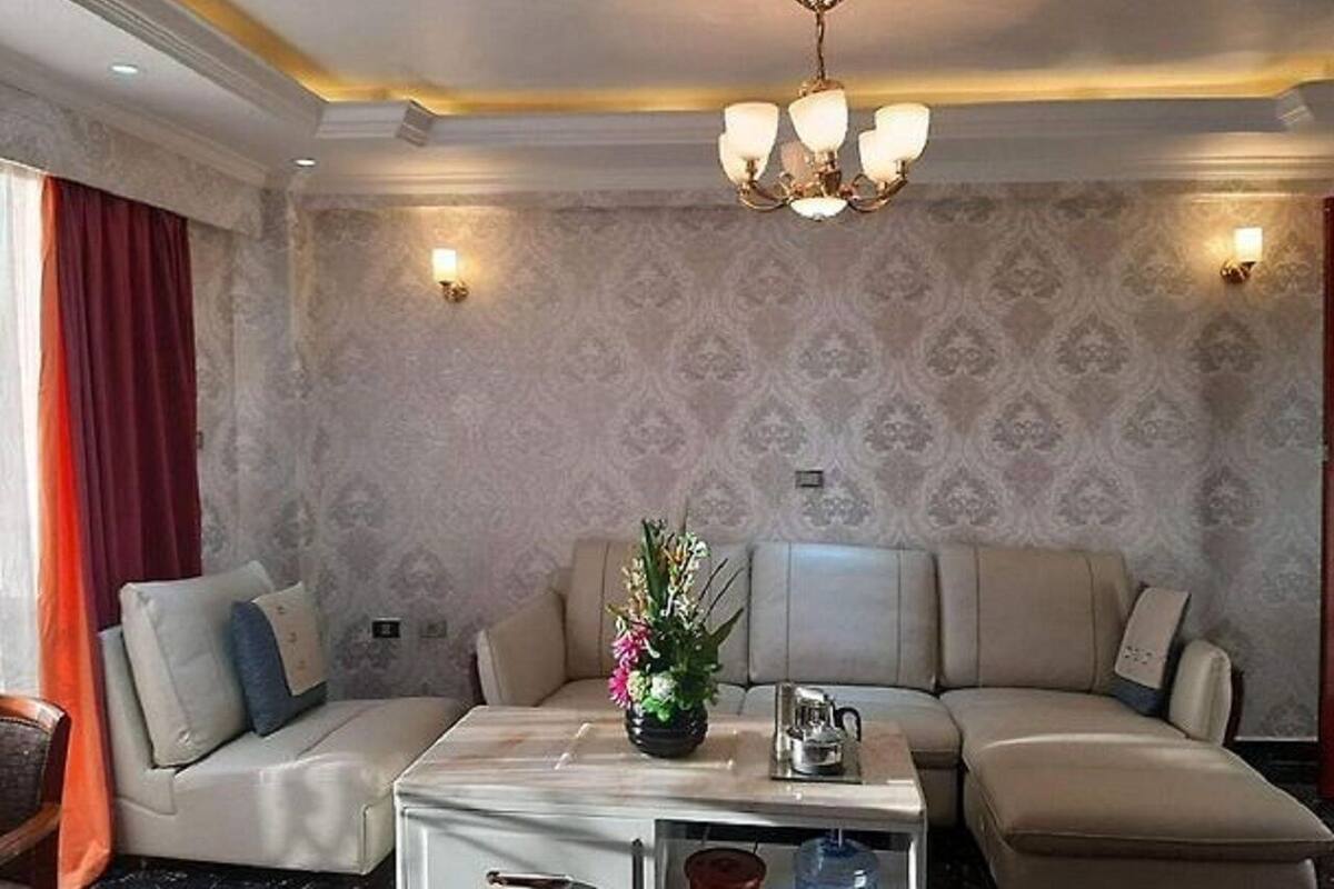 A modern living room with a beige sofa set, a white coffee table, and a chandelier.