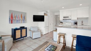 Una cocina moderna con armarios blancos, un televisor de pantalla plana y un comedor con taburetes.