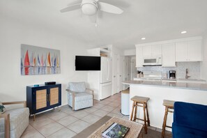 A modern kitchen with white cabinets, a flat-screen TV, and a dining area with stools. - Gorgeous Ocean Views Heated Pool Access (Tybee Island)