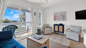 Una habitación con sofá, sillas, televisión, un cuadro y un balcón con vistas.