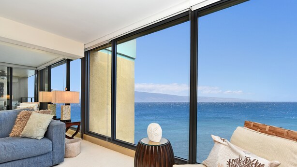 Un salon moderne avec une grande fenêtre donnant sur la mer, un canapé, une table d’appoint et une lampe.