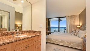 Une chambre d’hôtel dotée d’un grand lit, d’une salle de bain avec un lavabo au comptoir en granit et d’un balcon offrant une vue sur l’océan.